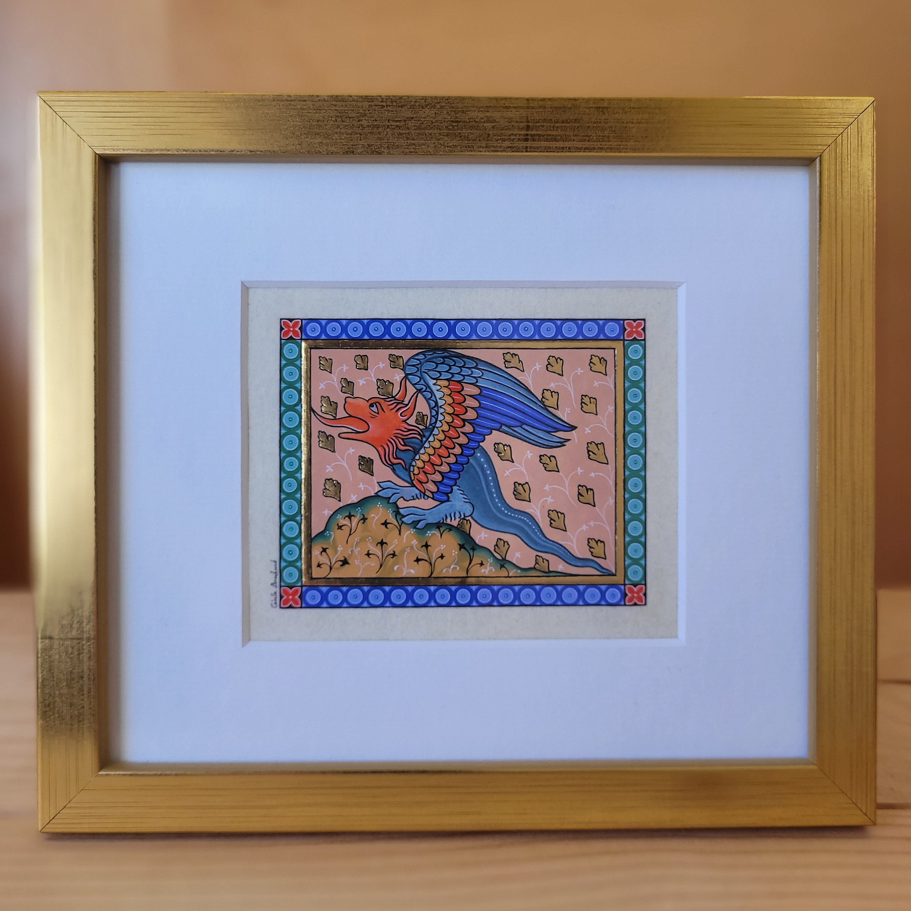 Enluminure médiévale de dragon sous cadre en bois doré.