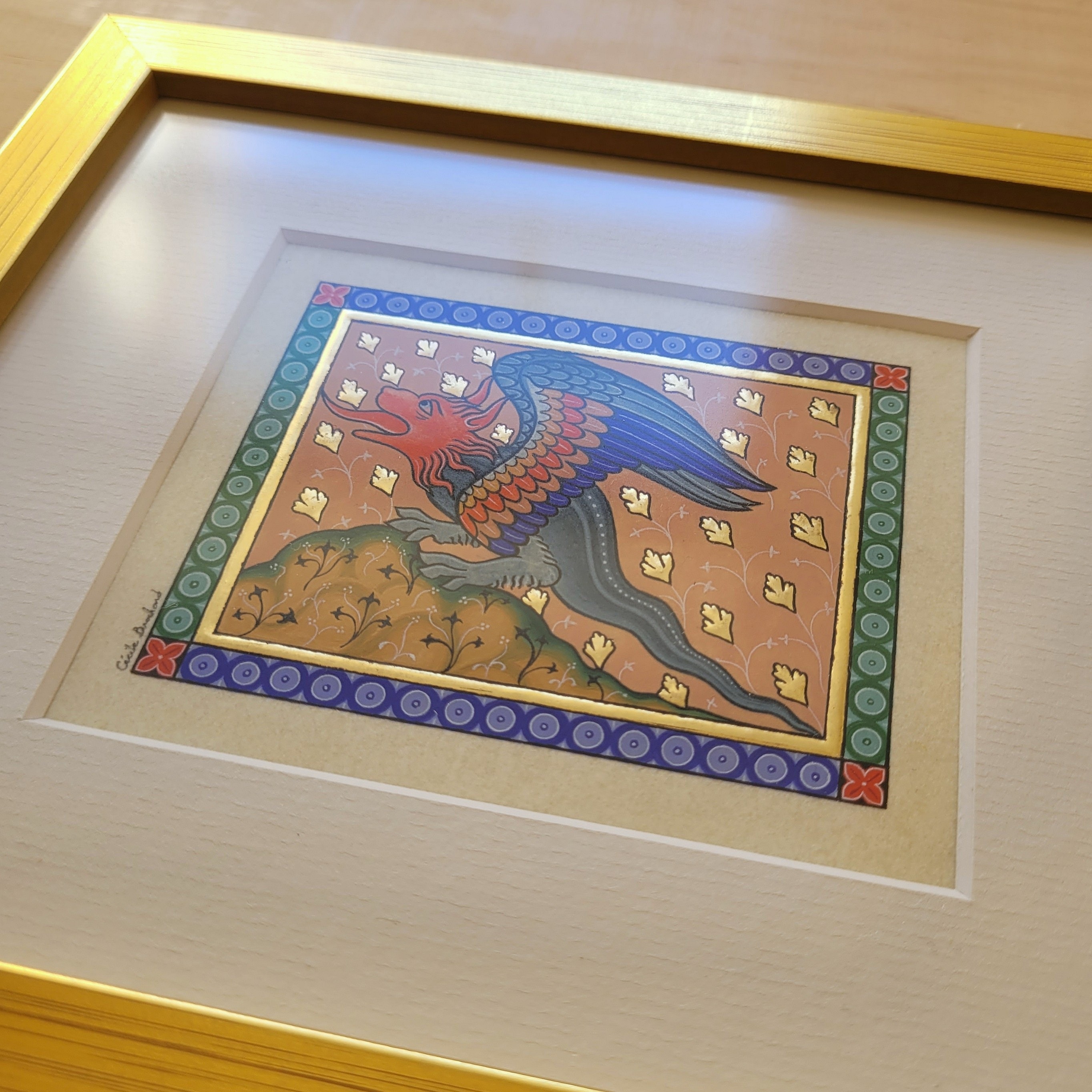 Enluminure médiévale d'un dragon sous cadre en bois doré.