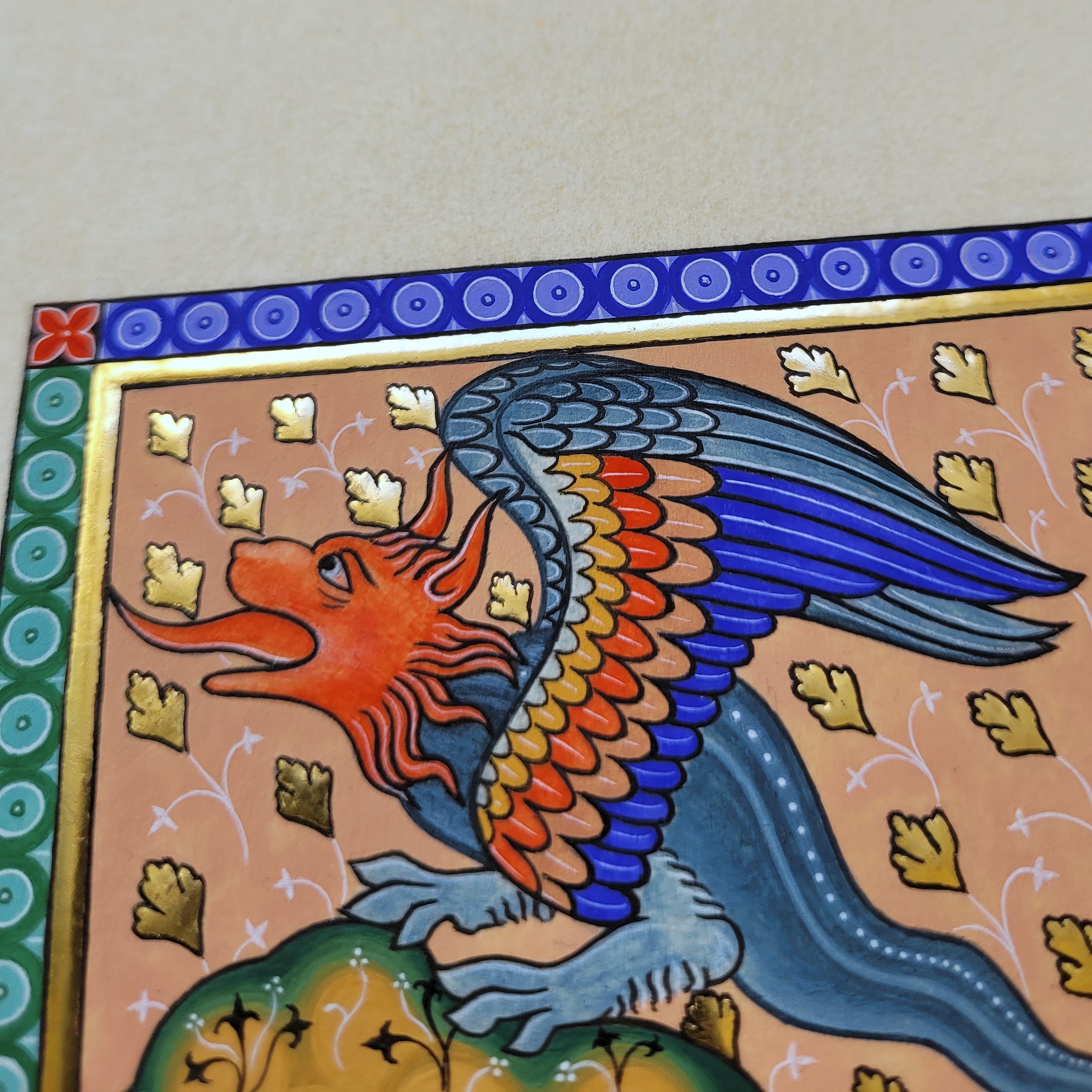 Enluminure médiévale d'un dragon coloré sur papier doré.