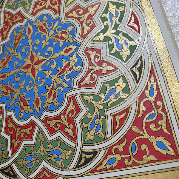 Enluminure marocaine authentique avec arabesques dorées, rouges, vertes et bleues.