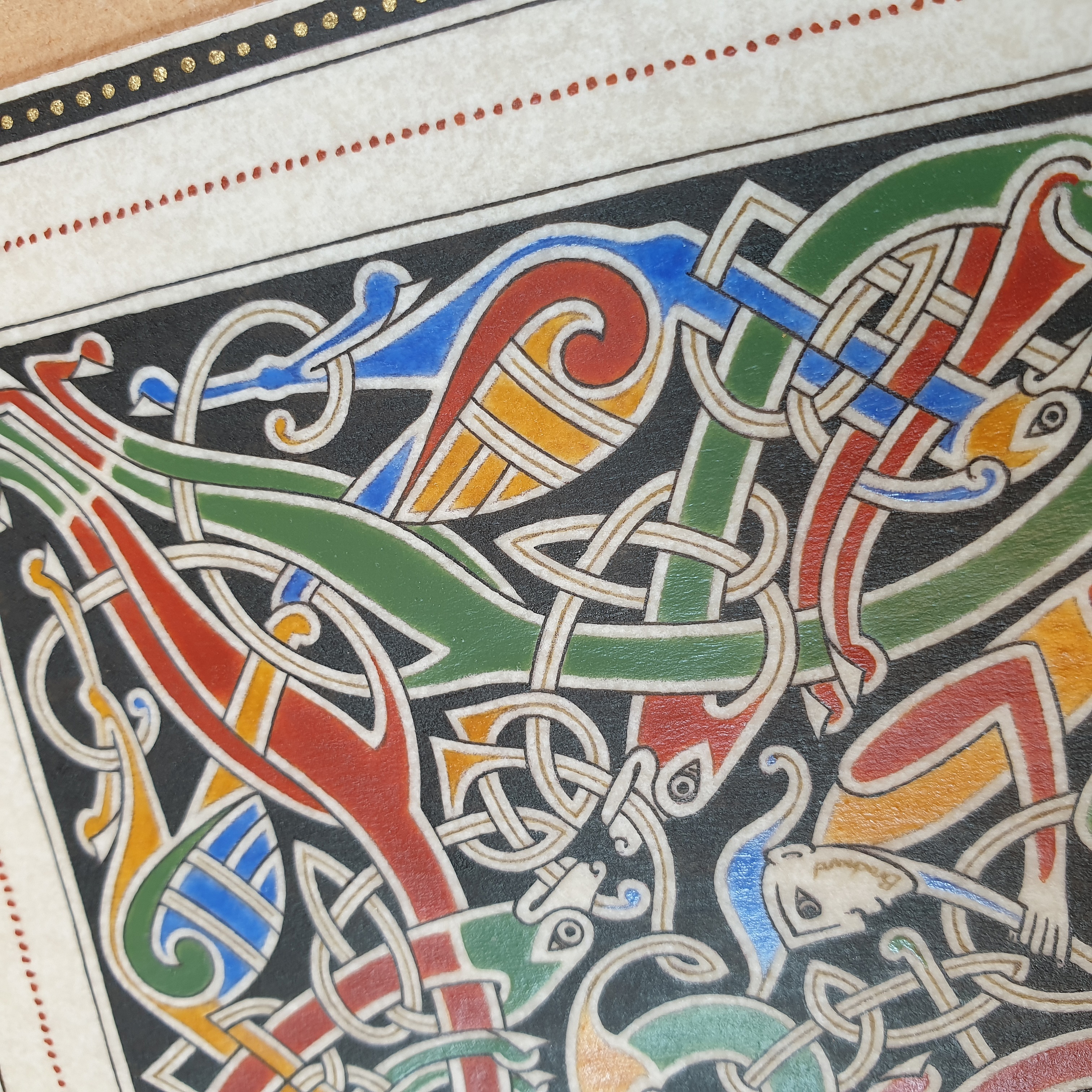 Enluminure insulaire avec entrelacs zoomorphes colorés sur fond noir.